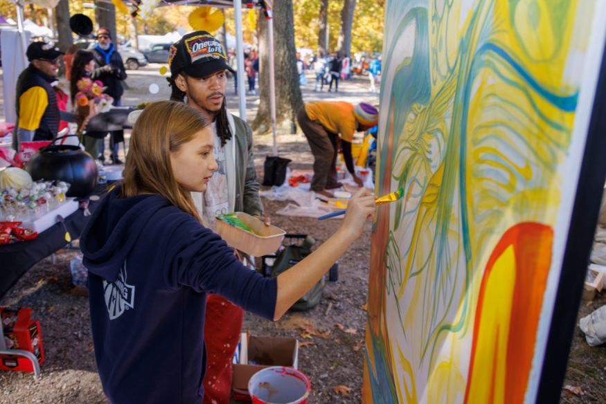 Rain Spann in hat helping young girl paint mural