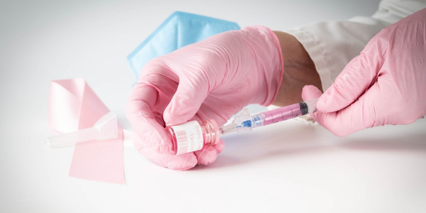 Pink gloved hands drawing up a dose of breast cancer vaccine from a glass vial, mock-up, pink vial.