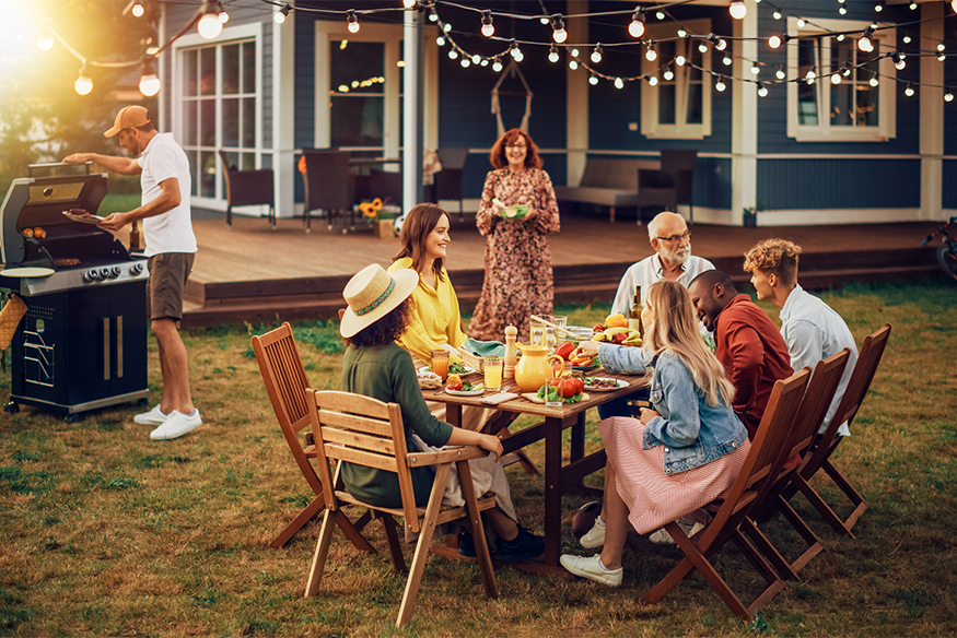 Photo of people gathered around a table in backyard sharing food