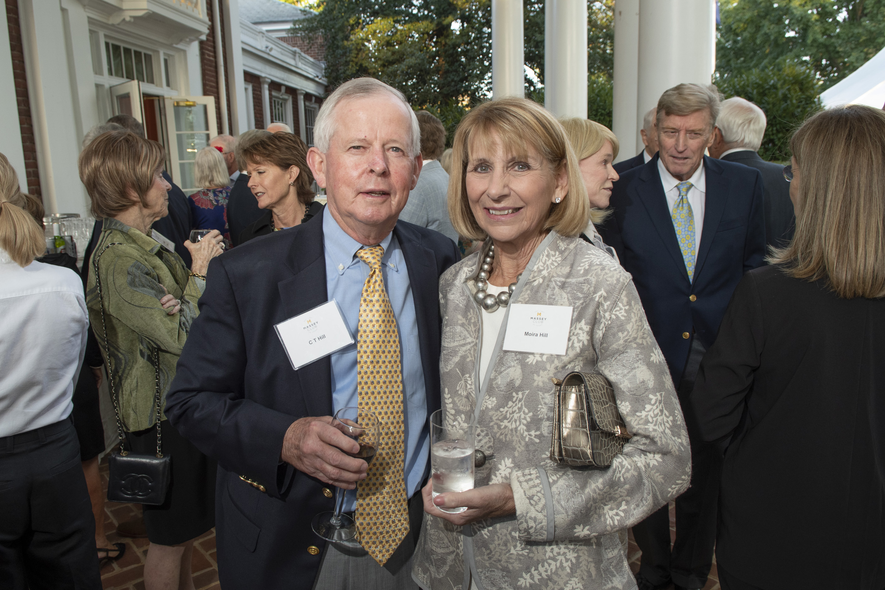A man and woman standing together at an outdoor evening event. Both are wearing name tags—
