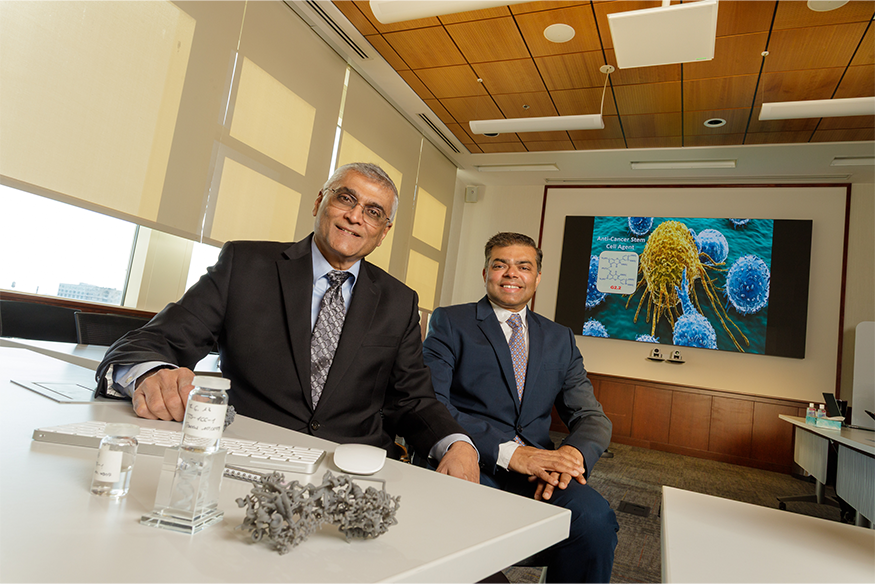 Two men sitting at a table smiling with miscellaneous scientific items on table