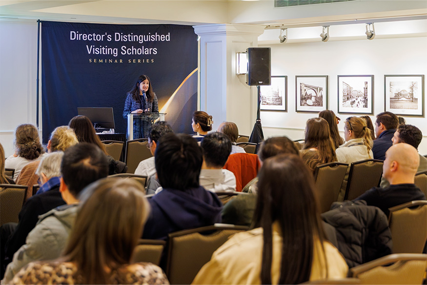 Woman standing at podium speaking to crowd of people
