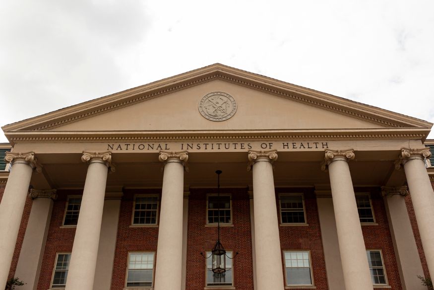 Exterior of the National Institutes of Health building featuring classical columns and a red brick facade.