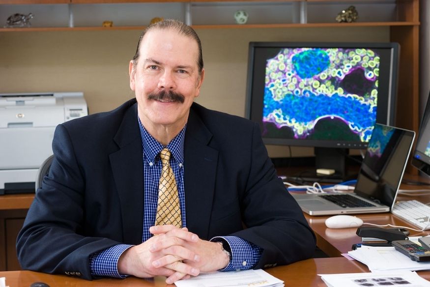 A white middle-aged male sitting at a desk with his hands crossed