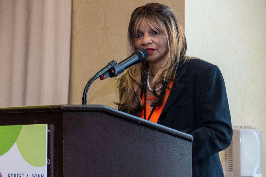 Photo of woman in suit speaking at a podium