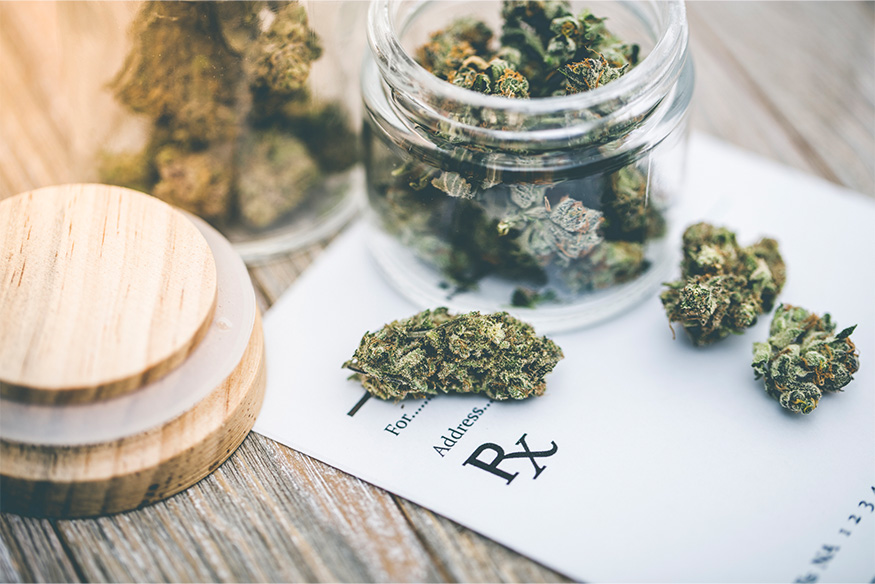 Dried cannabis buds in an open glass jar resting on a medical prescription pad with the Rx symbol.